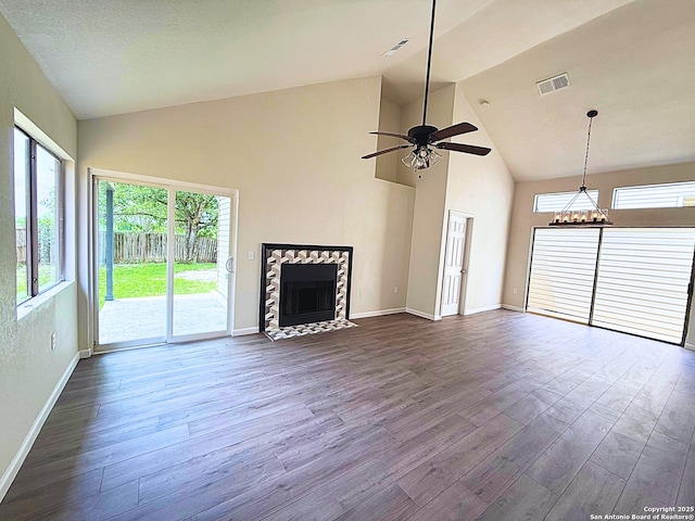 unfurnished living room featuring ceiling fan with notable chandelier, baseboards, a fireplace with flush hearth, dark wood-type flooring, and visible vents