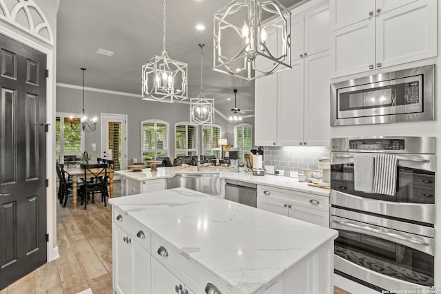 kitchen featuring appliances with stainless steel finishes, a sink, ceiling fan with notable chandelier, a center island, and a peninsula