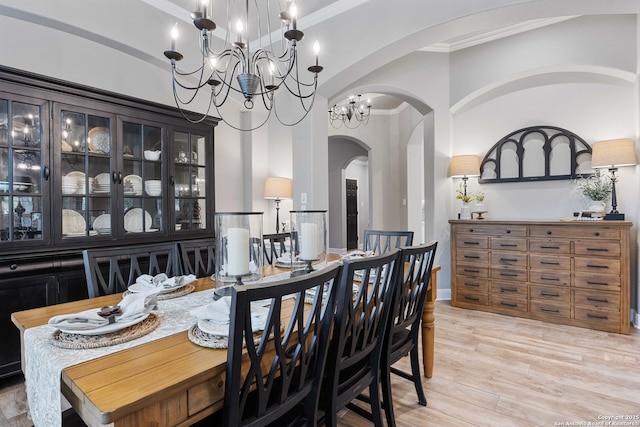 dining room with crown molding, arched walkways, light wood-type flooring, and a chandelier