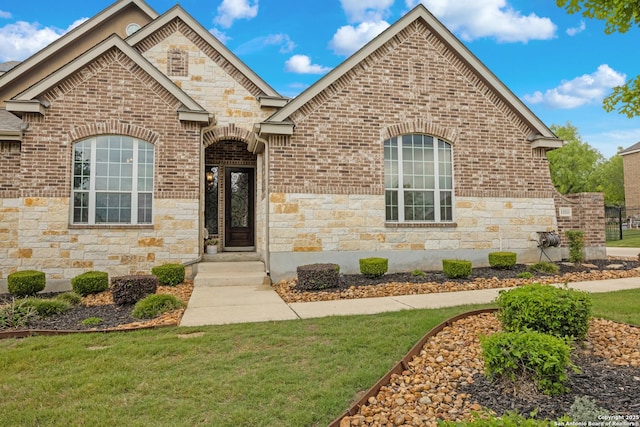 french provincial home with brick siding, a front lawn, and stone siding