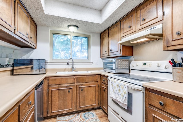 kitchen with appliances with stainless steel finishes, a sink, light countertops, brown cabinetry, and under cabinet range hood