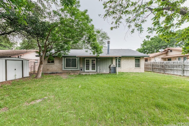 back of house featuring fence, a yard, french doors, brick siding, and a storage shed