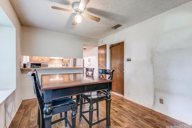 dining area featuring a ceiling fan, a textured ceiling, visible vents, wood finished floors, and baseboards