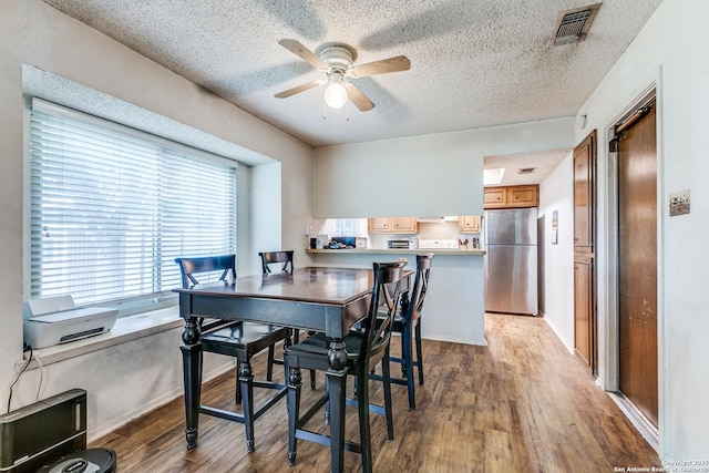 dining room featuring light wood-style flooring, a ceiling fan, a textured ceiling, and visible vents