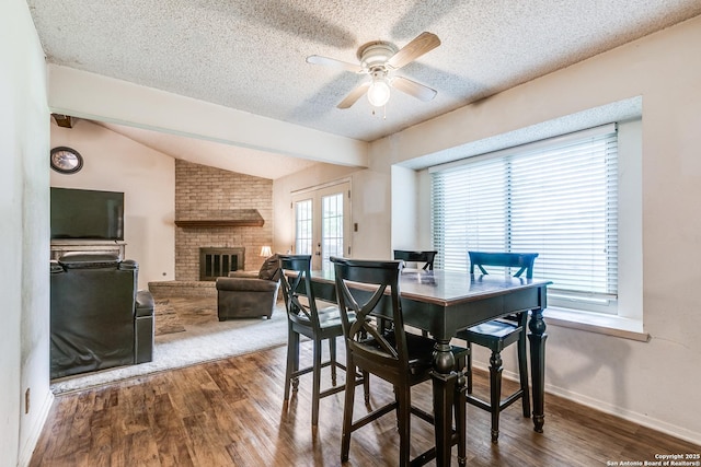 dining room featuring a textured ceiling, ceiling fan, a fireplace, and wood finished floors