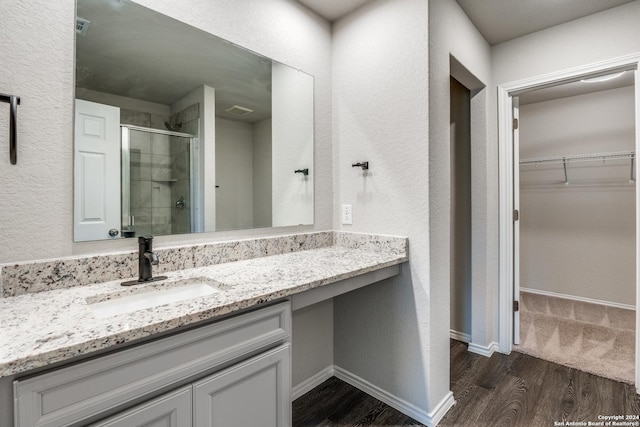 full bath with a walk in closet, a shower stall, wood finished floors, vanity, and baseboards