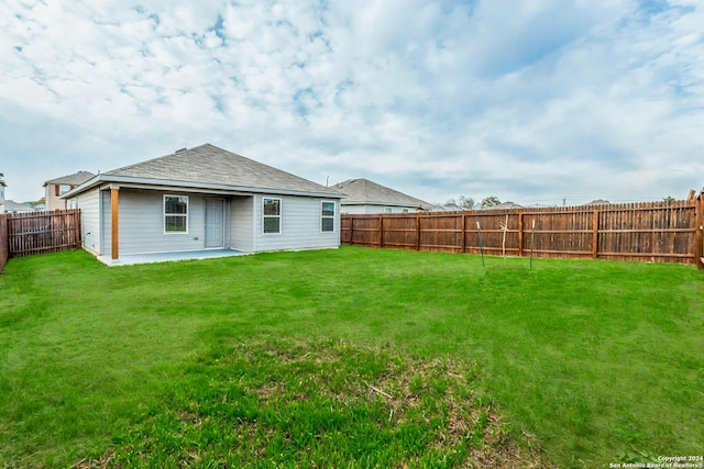 rear view of property featuring a yard, a patio, a fenced backyard, and roof with shingles