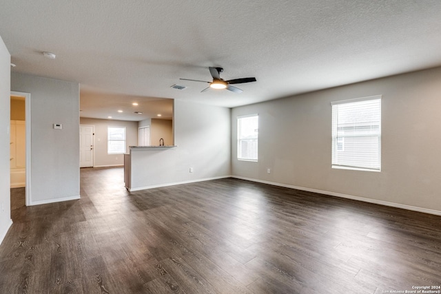 unfurnished living room featuring a ceiling fan, baseboards, a wealth of natural light, dark wood-type flooring, and visible vents
