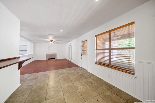 interior space with ceiling fan, a tiled fireplace, tile patterned flooring, a wainscoted wall, and recessed lighting