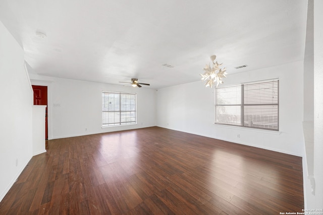 unfurnished room featuring baseboards, visible vents, dark wood-style floors, and ceiling fan with notable chandelier
