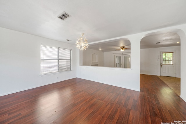 unfurnished living room with visible vents, wood finished floors, baseboards, arched walkways, and ceiling fan with notable chandelier
