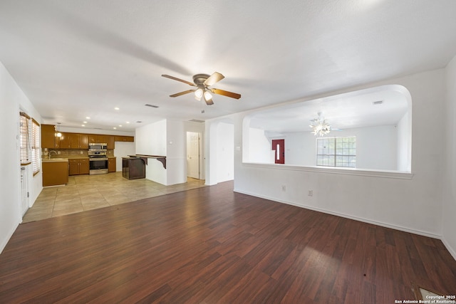 unfurnished living room featuring a sink, light wood-style flooring, ceiling fan with notable chandelier, recessed lighting, and baseboards