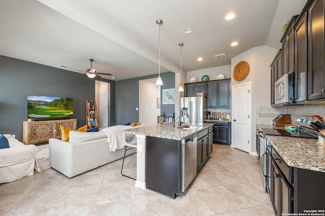 kitchen featuring open floor plan, appliances with stainless steel finishes, decorative backsplash, and light stone counters