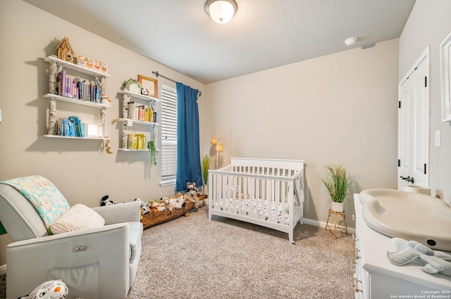 bedroom featuring a nursery area, baseboards, carpet flooring, and a textured ceiling