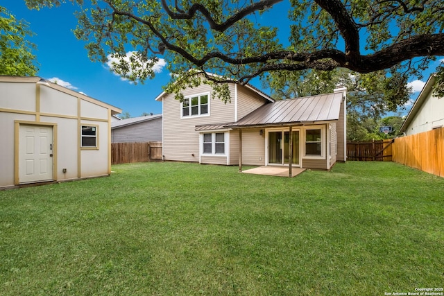 back of house with a fenced backyard, a yard, a chimney, and metal roof
