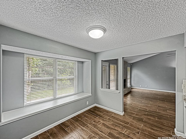 empty room with a textured ceiling, dark wood-style floors, baseboards, and a fireplace