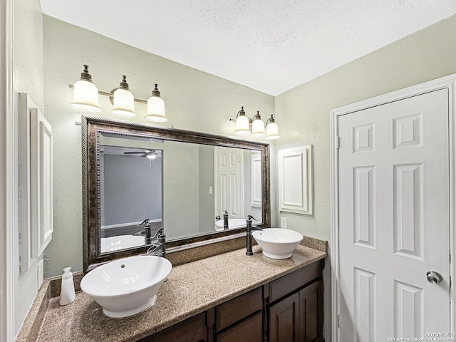 bathroom with double vanity, a ceiling fan, a sink, and a textured ceiling
