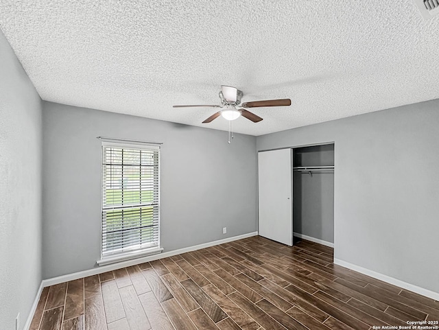 unfurnished bedroom with a closet, baseboards, ceiling fan, a textured ceiling, and dark wood finished floors