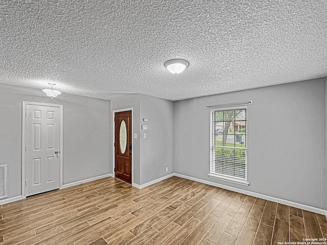 entrance foyer with a textured ceiling, baseboards, wood finished floors, and visible vents