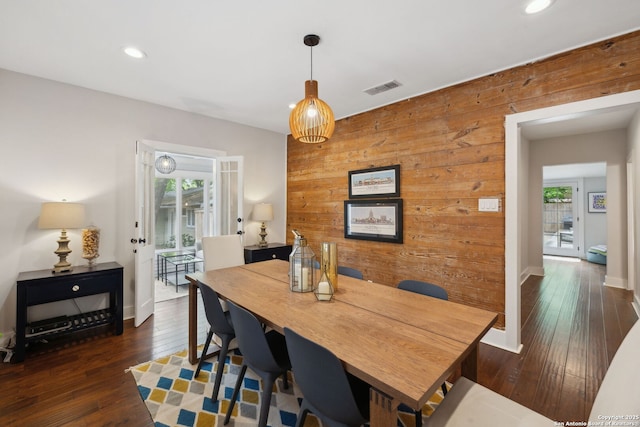 dining area with wood-type flooring, wooden walls, visible vents, and a healthy amount of sunlight