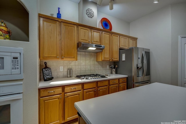 kitchen featuring light countertops, under cabinet range hood, brown cabinets, tasteful backsplash, and appliances with stainless steel finishes