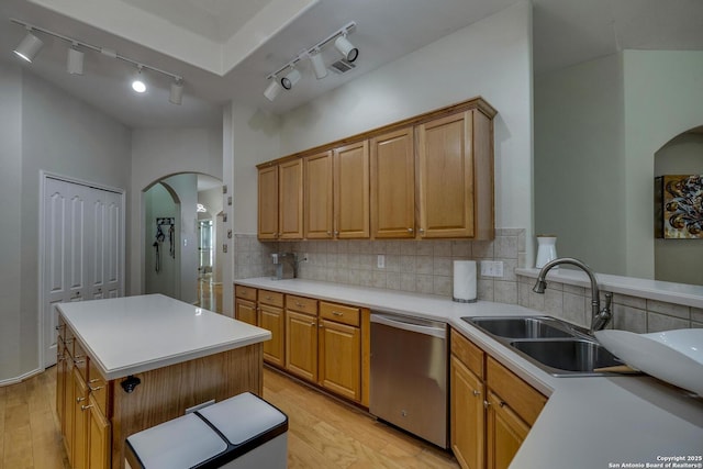 kitchen with a sink, dishwasher, light countertops, arched walkways, and light wood-style flooring