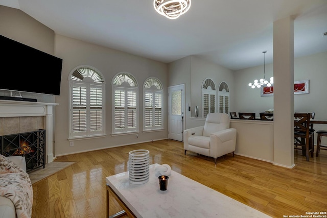 living area featuring baseboards, a tile fireplace, light wood-style flooring, and a notable chandelier