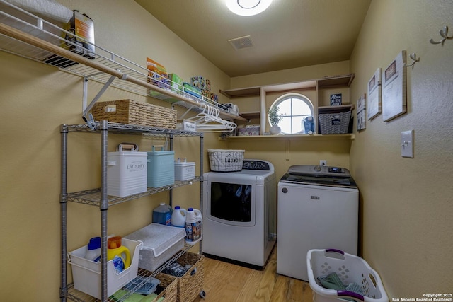 clothes washing area featuring independent washer and dryer, laundry area, visible vents, and wood finished floors