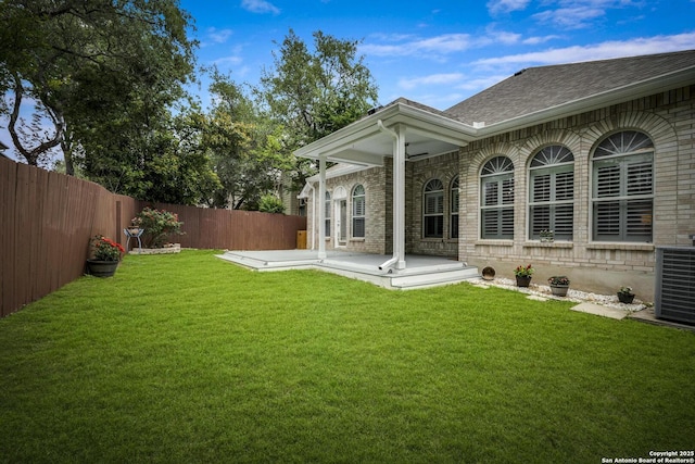 back of property with roof with shingles, brick siding, a fenced backyard, central AC unit, and a lawn