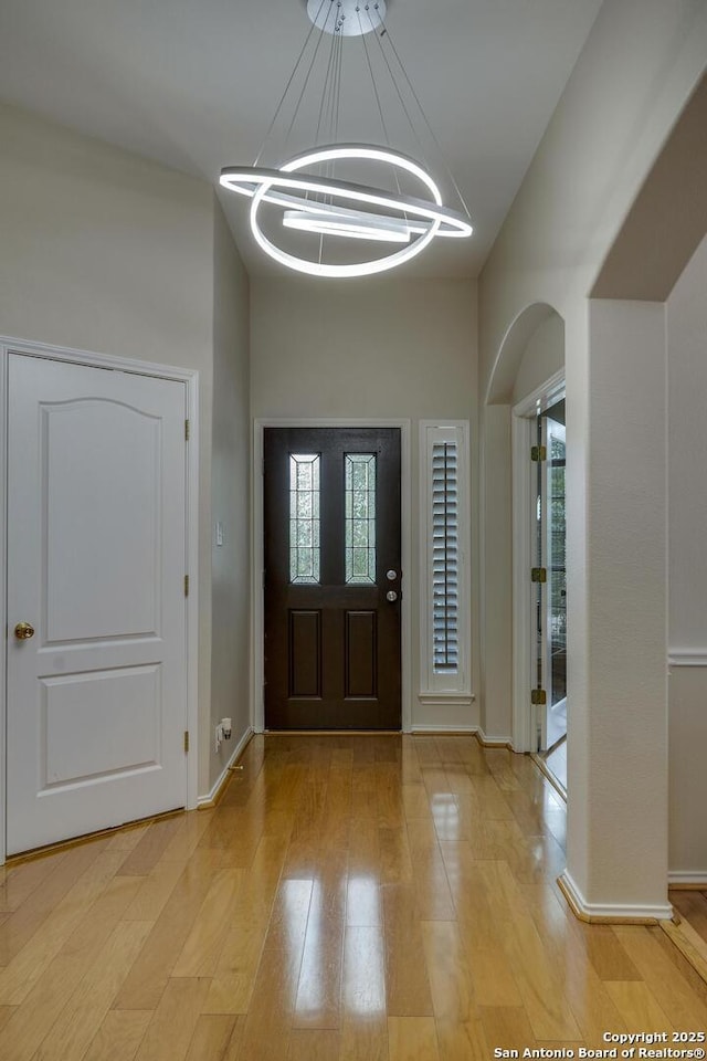 foyer entrance featuring light wood-style floors, baseboards, a healthy amount of sunlight, and an inviting chandelier
