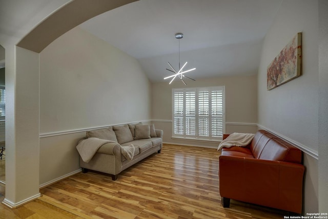 living area with an inviting chandelier, arched walkways, light wood-style flooring, baseboards, and lofted ceiling
