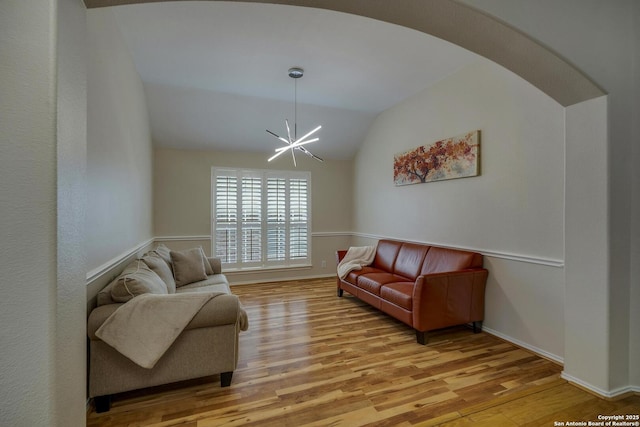 living area featuring baseboards, lofted ceiling, light wood-style flooring, and a notable chandelier