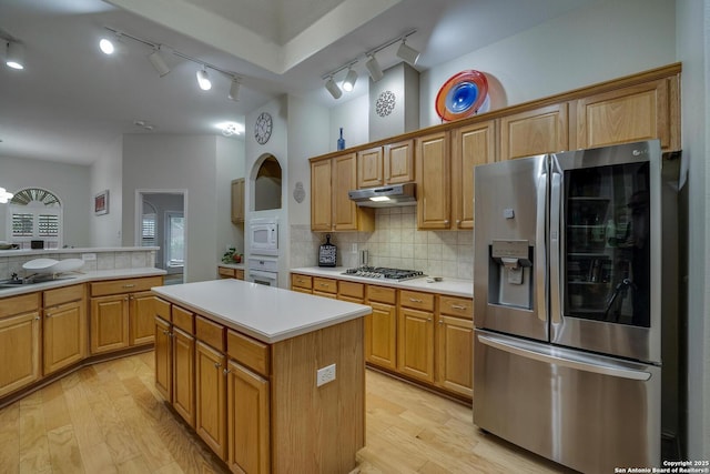 kitchen featuring light countertops, under cabinet range hood, rail lighting, light wood-style flooring, and stainless steel appliances