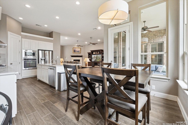dining space featuring dark wood-style flooring, ceiling fan, a fireplace, recessed lighting, and visible vents