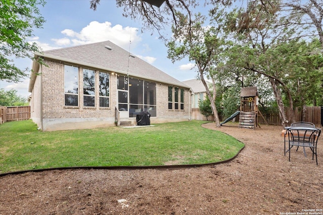 back of house featuring a fenced backyard, a lawn, a playground, and brick siding