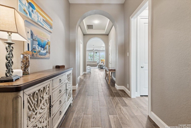 hall featuring visible vents, arched walkways, dark wood finished floors, baseboards, and a tray ceiling