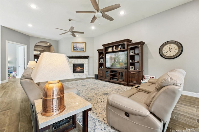 living area featuring baseboards, ceiling fan, a stone fireplace, and wood finished floors