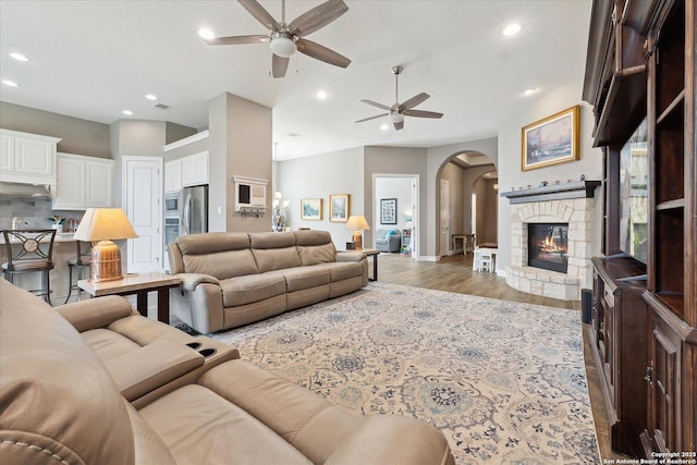 living area featuring a ceiling fan, arched walkways, a fireplace, light wood-type flooring, and recessed lighting