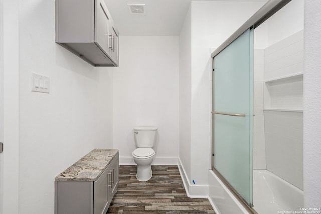 full bathroom with visible vents, wood finished floors, baseboards, bath / shower combo with glass door, and toilet
