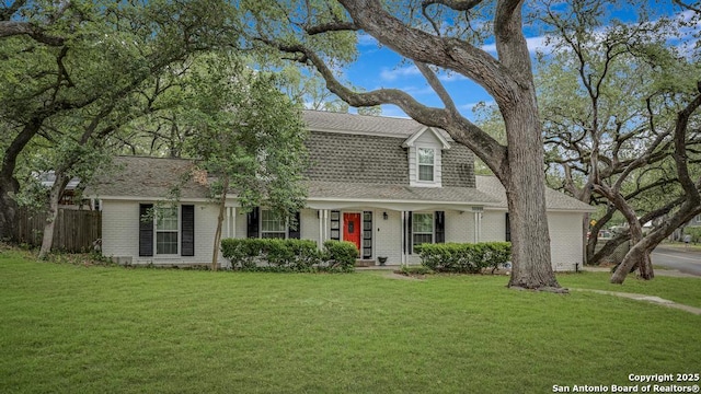 colonial inspired home featuring brick siding, fence, a shingled roof, and a front yard