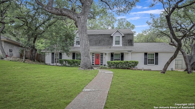 colonial inspired home with a shingled roof, a front lawn, and brick siding