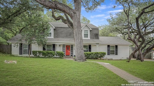 view of front of property featuring brick siding, a front lawn, roof with shingles, and fence