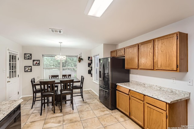 kitchen with stainless steel fridge, light tile patterned floors, brown cabinets, and decorative light fixtures