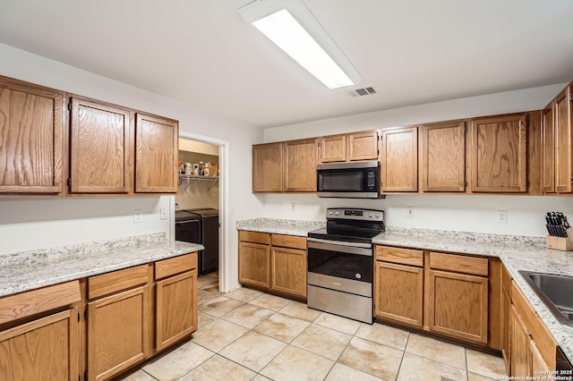 kitchen with brown cabinetry, appliances with stainless steel finishes, a sink, separate washer and dryer, and light tile patterned flooring