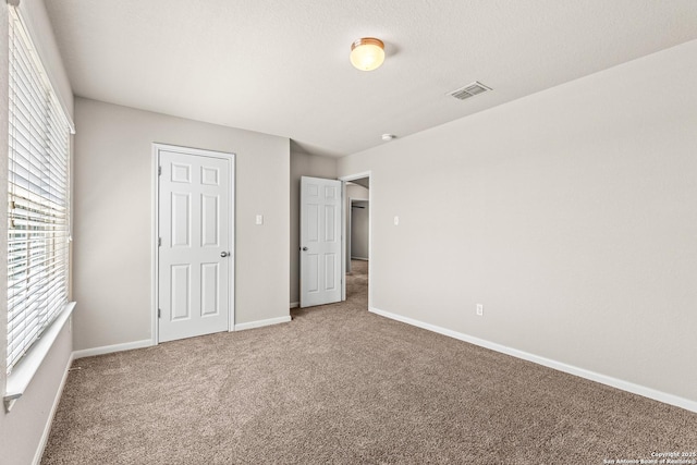 unfurnished bedroom with carpet floors, visible vents, and multiple windows