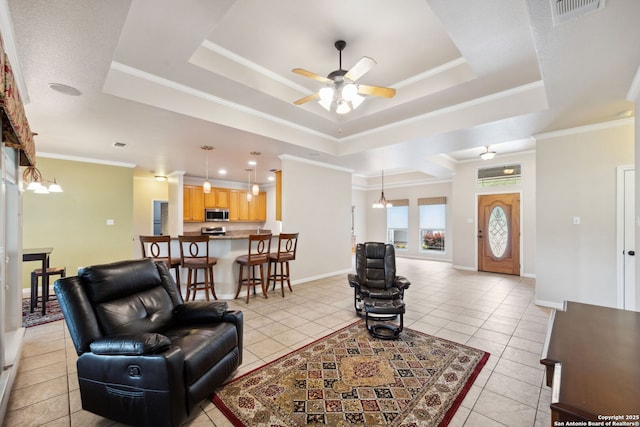 living area with a tray ceiling, visible vents, light tile patterned floors, and ceiling fan with notable chandelier