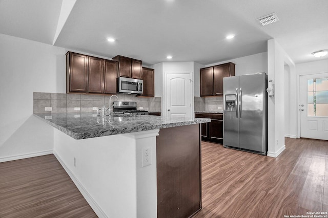kitchen featuring wood finished floors, a peninsula, dark brown cabinetry, and stainless steel appliances