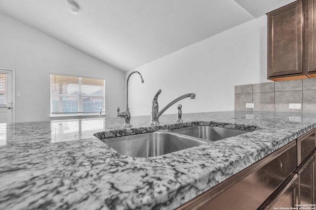 kitchen featuring a sink, a wealth of natural light, light stone countertops, and lofted ceiling