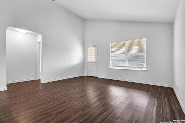 spare room featuring baseboards, dark wood-style floors, high vaulted ceiling, and arched walkways