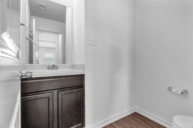 bathroom featuring vanity, toilet, baseboards, wood finished floors, and visible vents
